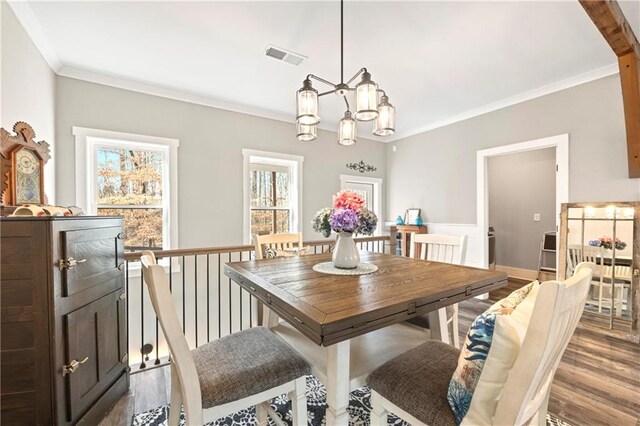 dining space with a notable chandelier, wood finished floors, visible vents, and crown molding