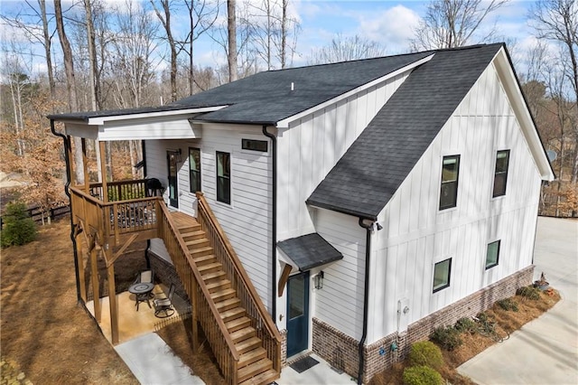 view of front of house with a shingled roof, stairway, a patio area, board and batten siding, and brick siding