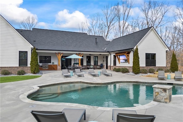 back of property featuring a patio area, brick siding, an outdoor pool, and roof with shingles