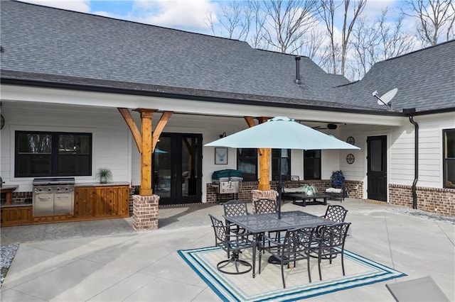 back of house with outdoor dining area, brick siding, area for grilling, roof with shingles, and a patio area