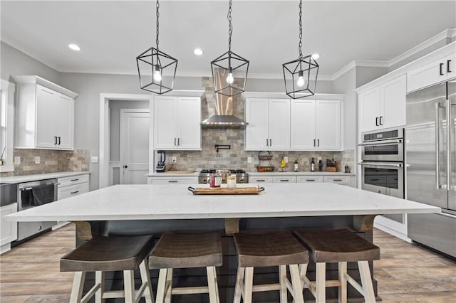 kitchen featuring wall chimney range hood, a large island, appliances with stainless steel finishes, and a breakfast bar area