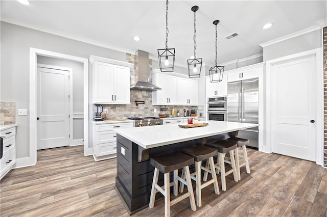 kitchen with stainless steel appliances, light countertops, white cabinets, wall chimney range hood, and a kitchen bar