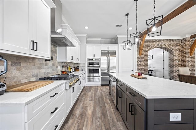 kitchen featuring hanging light fixtures, wall chimney range hood, appliances with stainless steel finishes, and white cabinetry