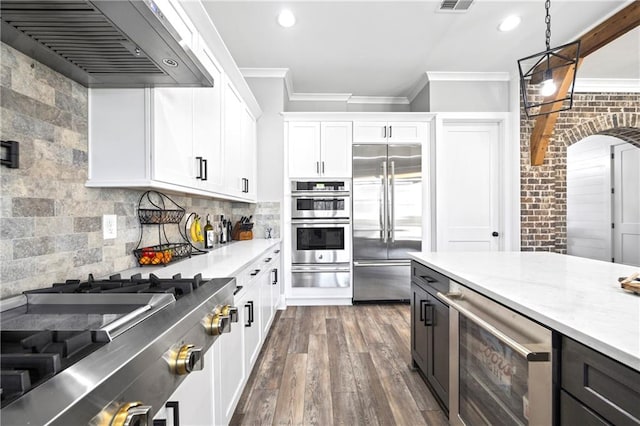 kitchen featuring beverage cooler, appliances with stainless steel finishes, wall chimney range hood, white cabinetry, and pendant lighting