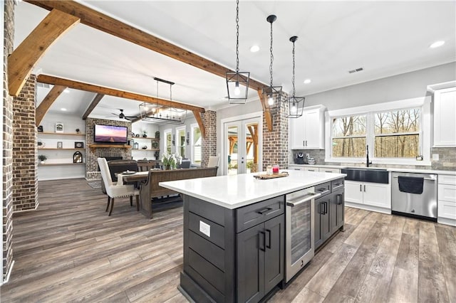 kitchen featuring light countertops, stainless steel dishwasher, open floor plan, white cabinets, and a sink