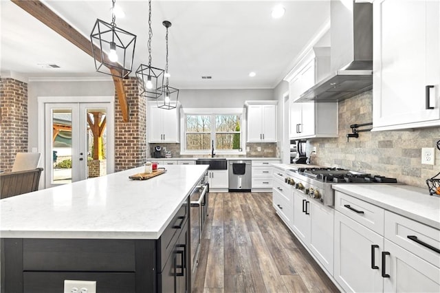 kitchen featuring stainless steel gas cooktop, a kitchen island, white cabinetry, french doors, and wall chimney exhaust hood