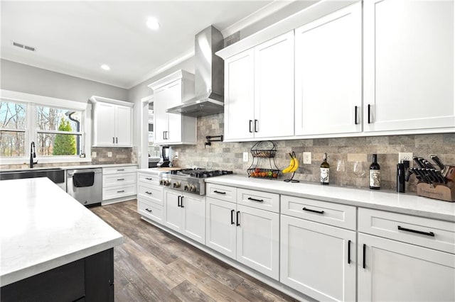 kitchen with a sink, white cabinetry, appliances with stainless steel finishes, wall chimney exhaust hood, and tasteful backsplash