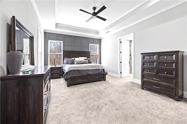 bedroom featuring ornamental molding, a tray ceiling, light carpet, and baseboards