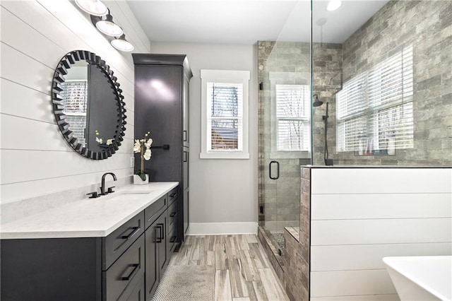 full bathroom with baseboards, wood finished floors, vanity, a freestanding tub, and a shower stall