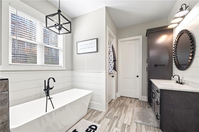 full bath with a soaking tub, a chandelier, wood finished floors, and vanity