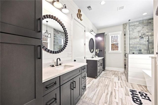 full bath featuring a stall shower, visible vents, wood finished floors, a sink, and two vanities