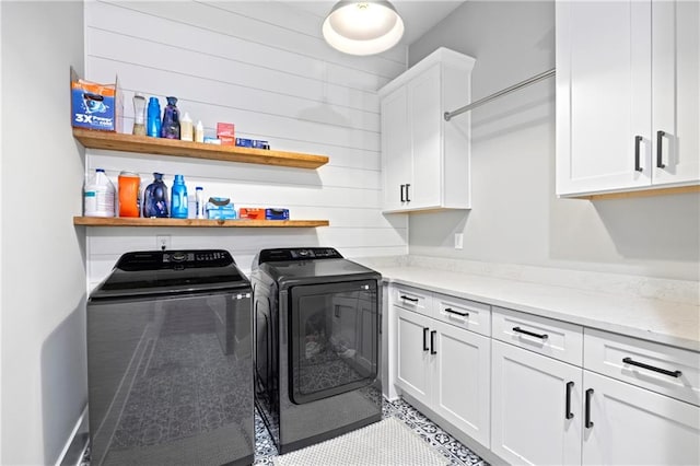 clothes washing area with cabinet space, wooden walls, and washer and dryer