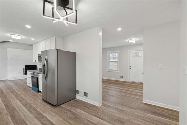 1573 Deerwood Ln, Acworth, GA 30102 - kitchen featuring white cabinets, light wood-type flooring, stainless steel appliances, and a brick fireplace