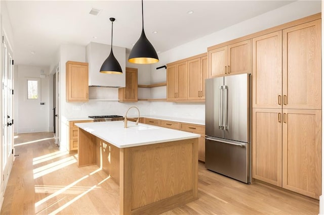 kitchen with sink, decorative light fixtures, a center island with sink, light wood-type flooring, and appliances with stainless steel finishes