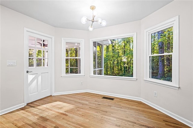 unfurnished dining area featuring light wood-type flooring, visible vents, a notable chandelier, and baseboards