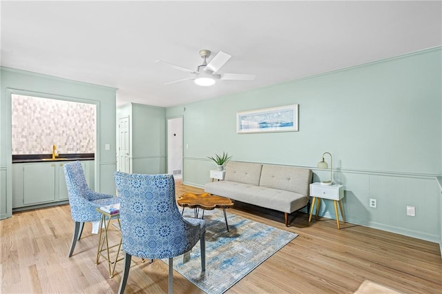 living area with light wood-style floors, wainscoting, and a ceiling fan