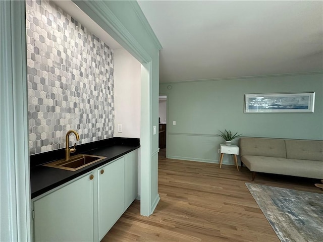 kitchen featuring tasteful backsplash, baseboards, dark countertops, light wood-style floors, and a sink