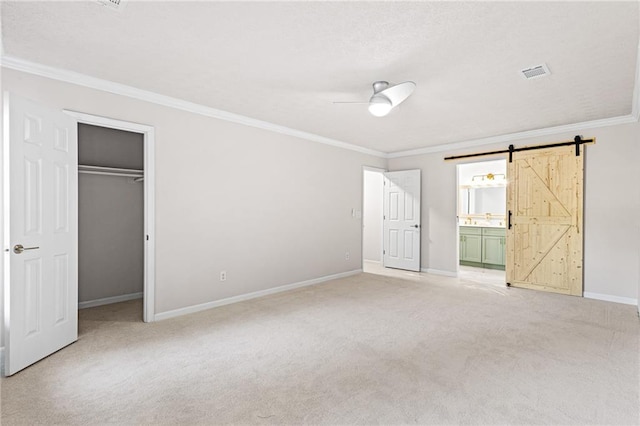 unfurnished bedroom featuring a barn door, light colored carpet, visible vents, baseboards, and crown molding