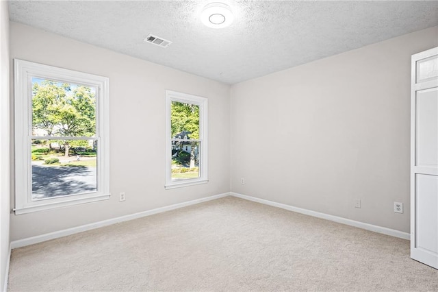 spare room with light carpet, baseboards, visible vents, and a textured ceiling