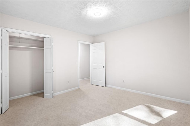 unfurnished bedroom featuring light carpet, a textured ceiling, baseboards, and a closet