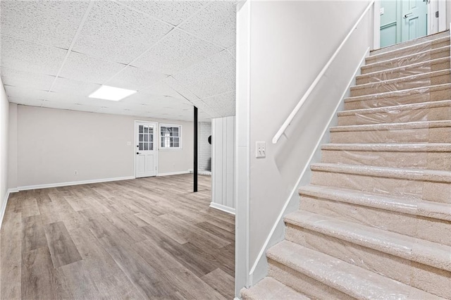 staircase featuring a paneled ceiling, baseboards, and wood finished floors