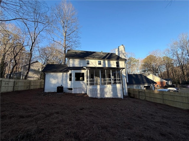 rear view of house with a sunroom, a fenced backyard, and a chimney