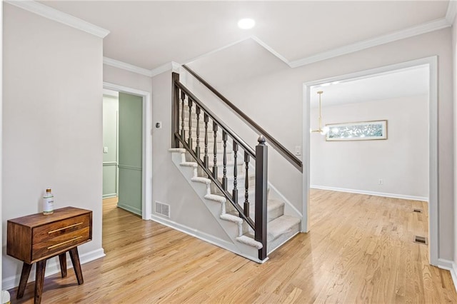 staircase with ornamental molding, wood finished floors, visible vents, and baseboards