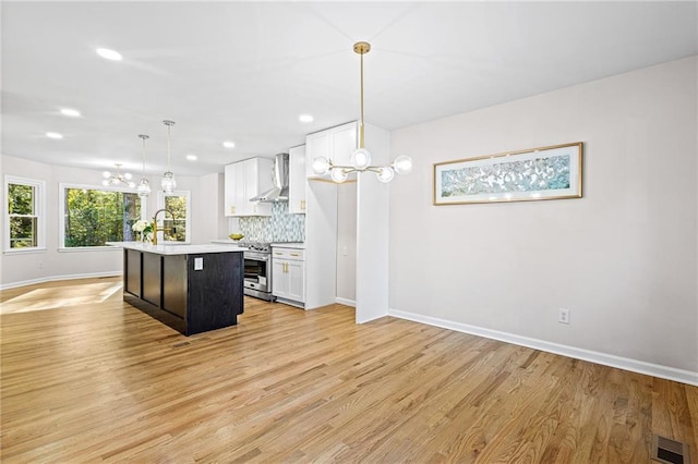 kitchen with white cabinets, stainless steel range oven, light countertops, wall chimney exhaust hood, and decorative light fixtures