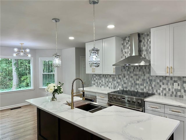 kitchen featuring white cabinets, wall chimney exhaust hood, decorative light fixtures, high end stainless steel range, and a sink