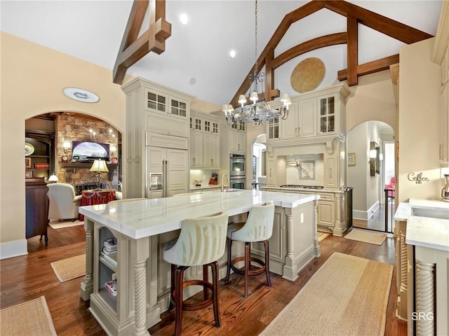 kitchen featuring glass insert cabinets, arched walkways, a large island with sink, and decorative light fixtures