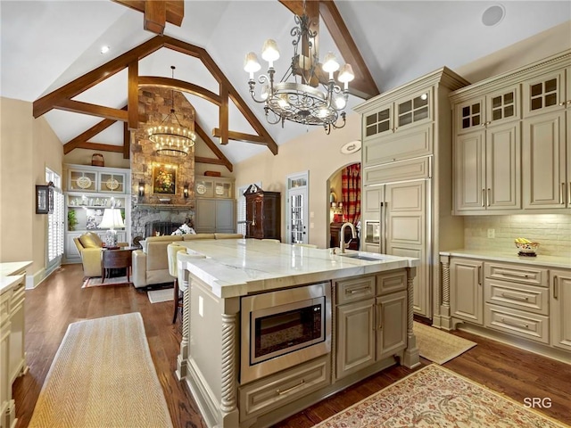 kitchen with stainless steel microwave, cream cabinets, open floor plan, an island with sink, and a chandelier