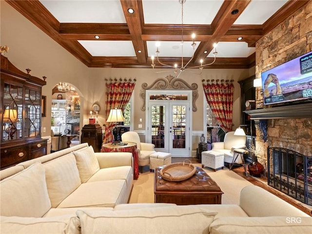 living room featuring coffered ceiling, french doors, an inviting chandelier, a stone fireplace, and beam ceiling