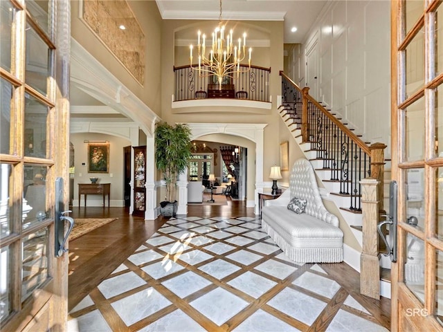 foyer featuring arched walkways, a notable chandelier, baseboards, stairway, and crown molding