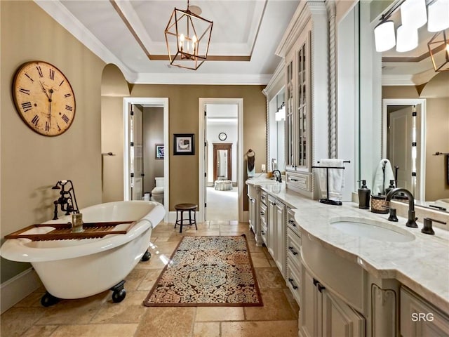 full bathroom featuring stone tile floors, a freestanding bath, ornamental molding, double vanity, and a raised ceiling