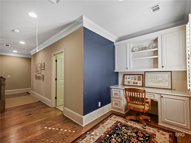 office featuring dark wood-style flooring, visible vents, baseboards, ornamental molding, and built in desk