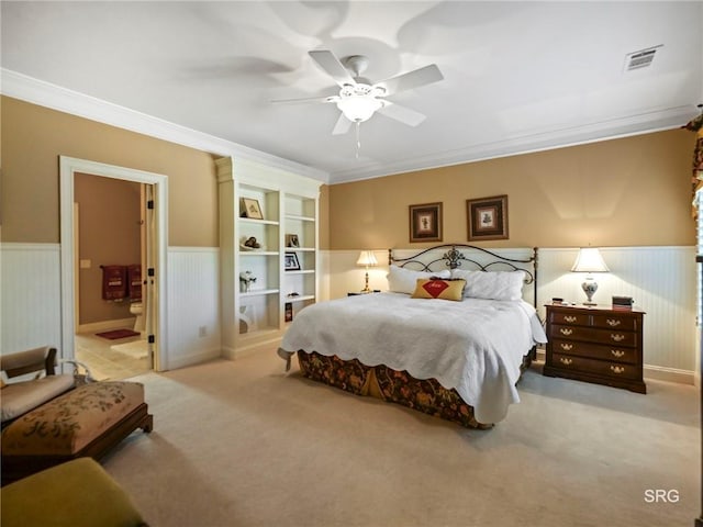 bedroom with ornamental molding, visible vents, light colored carpet, and wainscoting