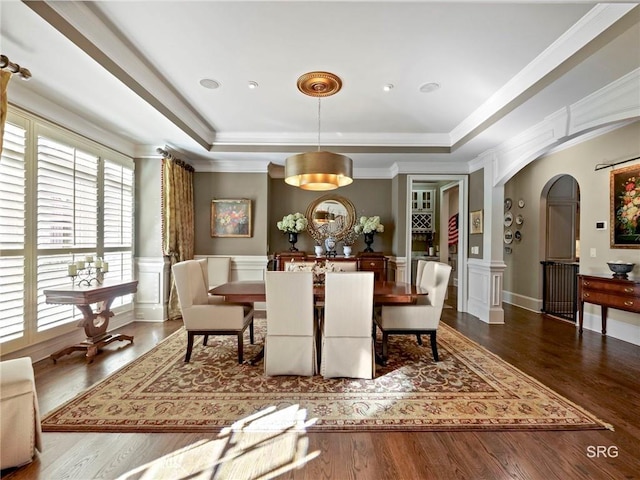 dining space with a tray ceiling, wainscoting, a decorative wall, and arched walkways