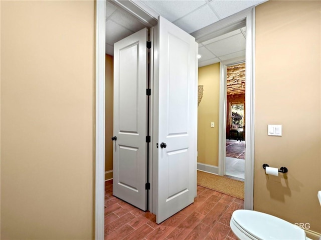 bathroom featuring baseboards, a drop ceiling, toilet, and wood tiled floor