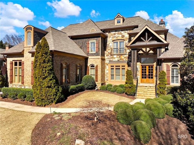 french country style house with a shingled roof, french doors, brick siding, and stone siding