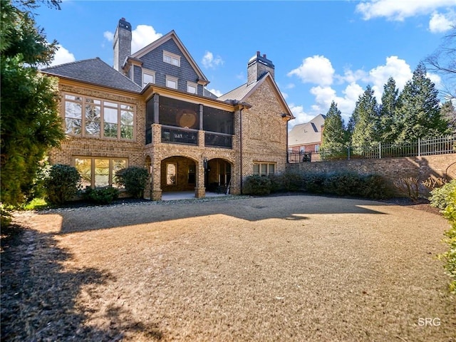 back of property with a sunroom, brick siding, fence, and a chimney