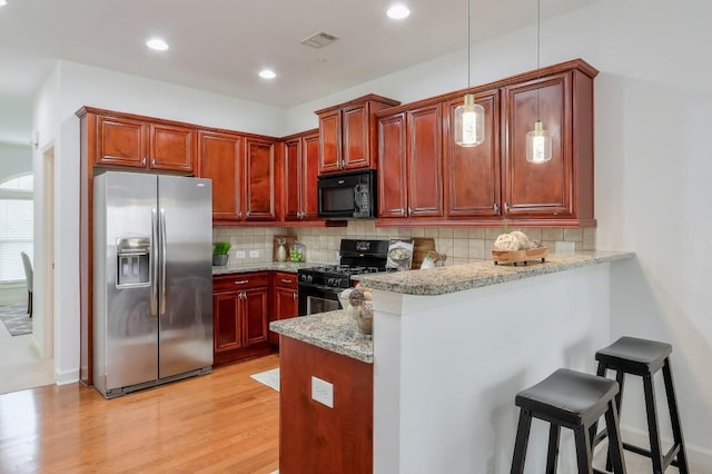 kitchen featuring a breakfast bar area, backsplash, a peninsula, and black appliances