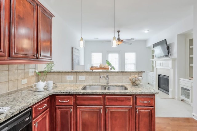 kitchen with reddish brown cabinets, black dishwasher, a sink, light stone countertops, and backsplash