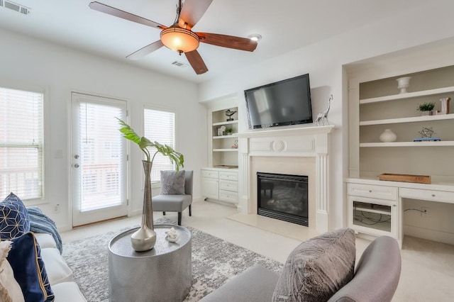 living room with built in features, visible vents, a ceiling fan, a high end fireplace, and light carpet