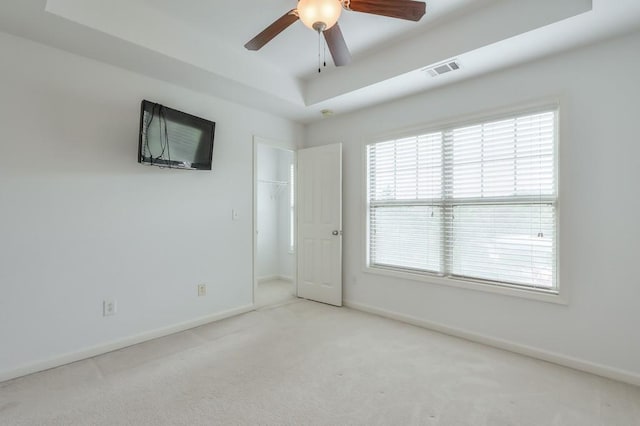 empty room with carpet, a raised ceiling, visible vents, a ceiling fan, and baseboards