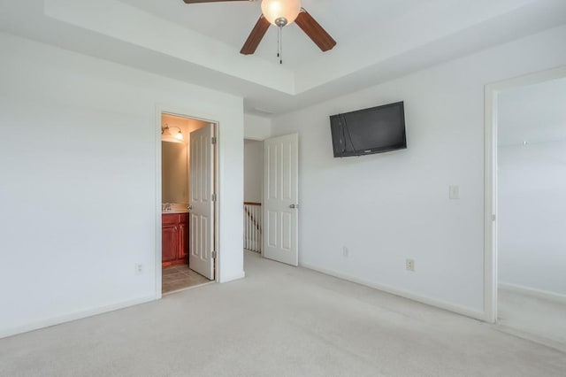 unfurnished bedroom featuring light colored carpet, baseboards, a closet, a tray ceiling, and a walk in closet