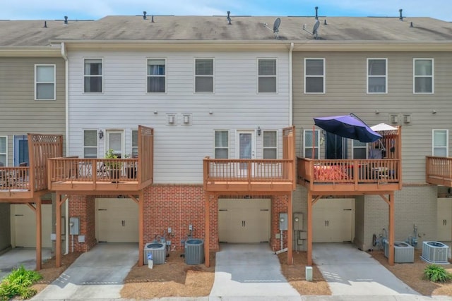 rear view of house featuring a garage, concrete driveway, central AC, and brick siding