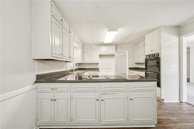 2466 Country Club Dr, Conyers, GA 30013 - kitchen with black appliances, a peninsula, dark wood-style flooring, white cabinets, and wainscoting