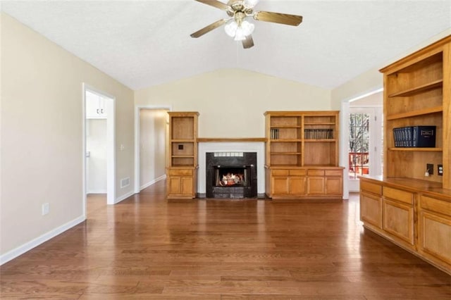 living area with a lit fireplace, a ceiling fan, vaulted ceiling, and wood finished floors