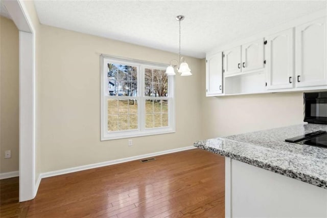 kitchen with wood-type flooring, light stone countertops, visible vents, and white cabinets