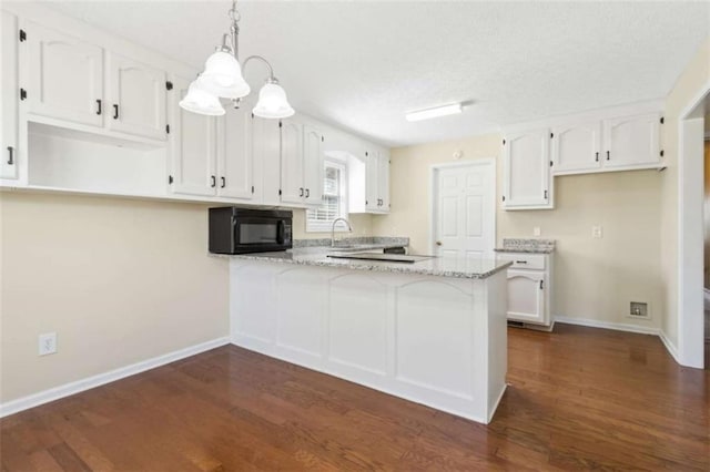 kitchen with black microwave, white cabinetry, a sink, and a peninsula